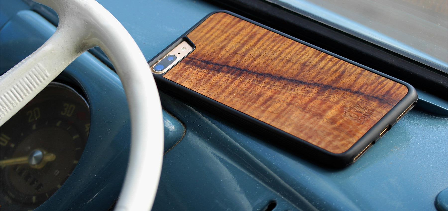 hand made Koa wood phone case with amazing curly grain pattern set on the dash of a dove blue vintage vw bus