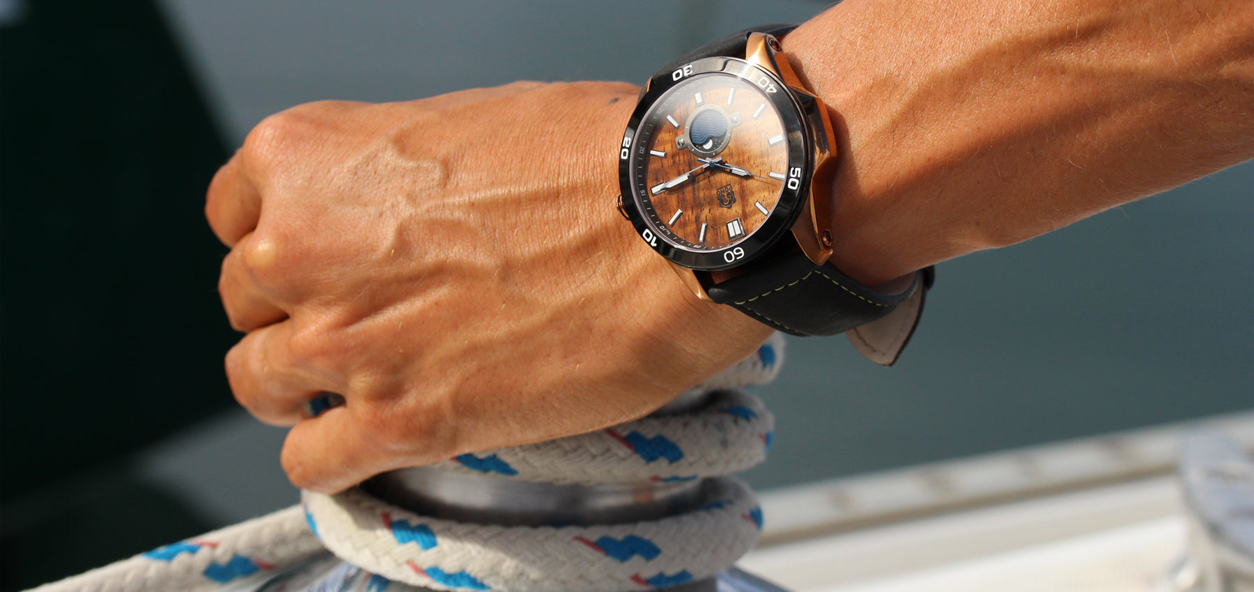 waterproof wood watch with stainless body closeup on mans wrist as he works the winch and lines of a sailboat