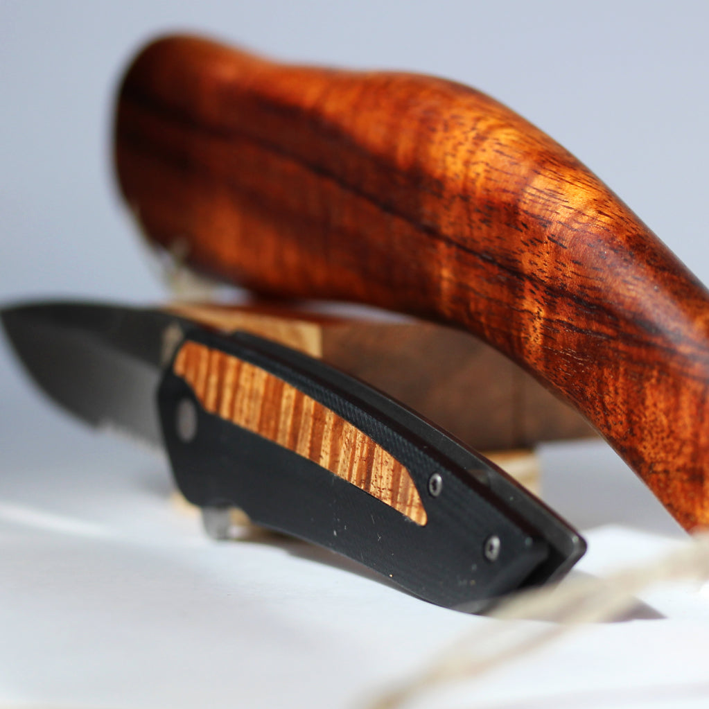 koa wood pocket knife set on edge parallel to ancient Hawaiian weapon showing the similarity in shape
