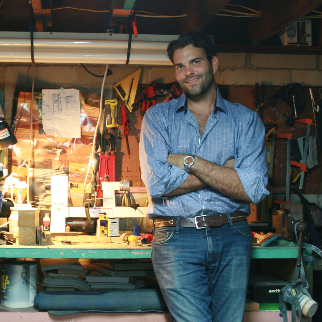 Brett Gontarek, Founder of Pono Woodworks smiling with arms folded and leaning casually against his workbench in his shop