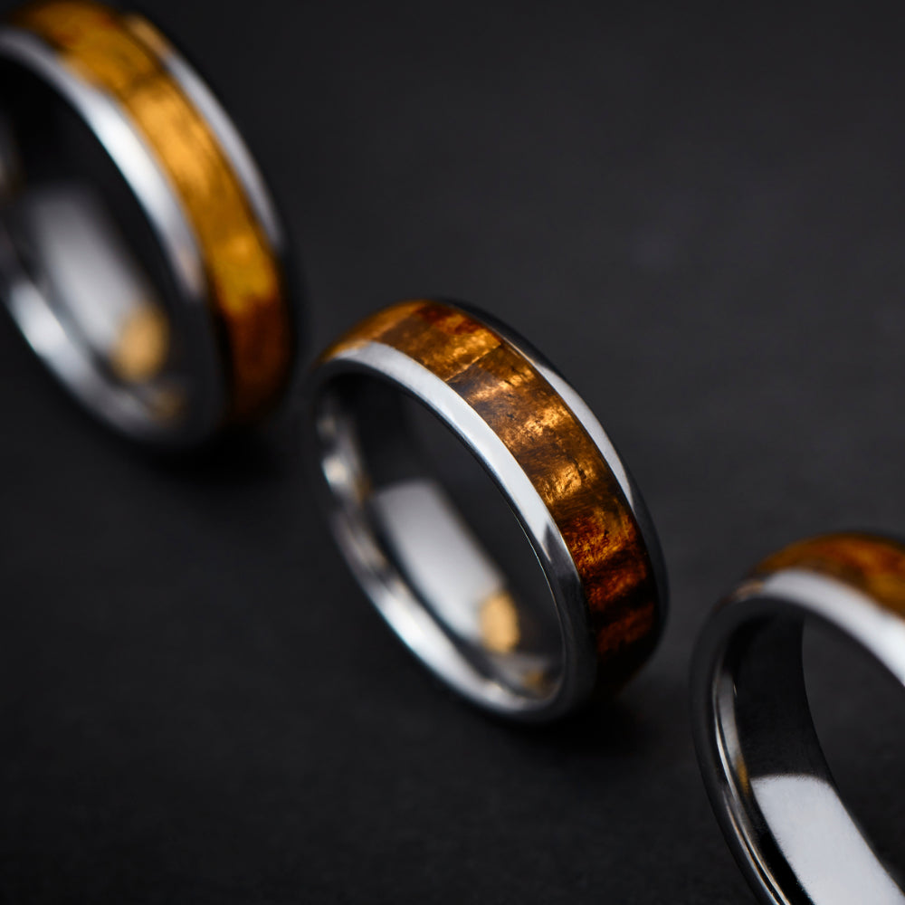three insanely curly koa wood and tungsten finger rings lined up and standing on edge with a black background