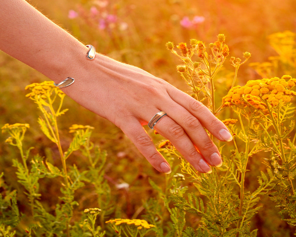 closeup of women's hand floating through sunkissed yellow flowers with a koa wood cuff and ring on