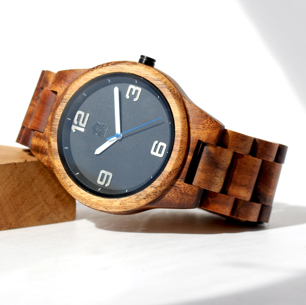 round shape solid koa wood watch with simple black face leaning up on small block of wood